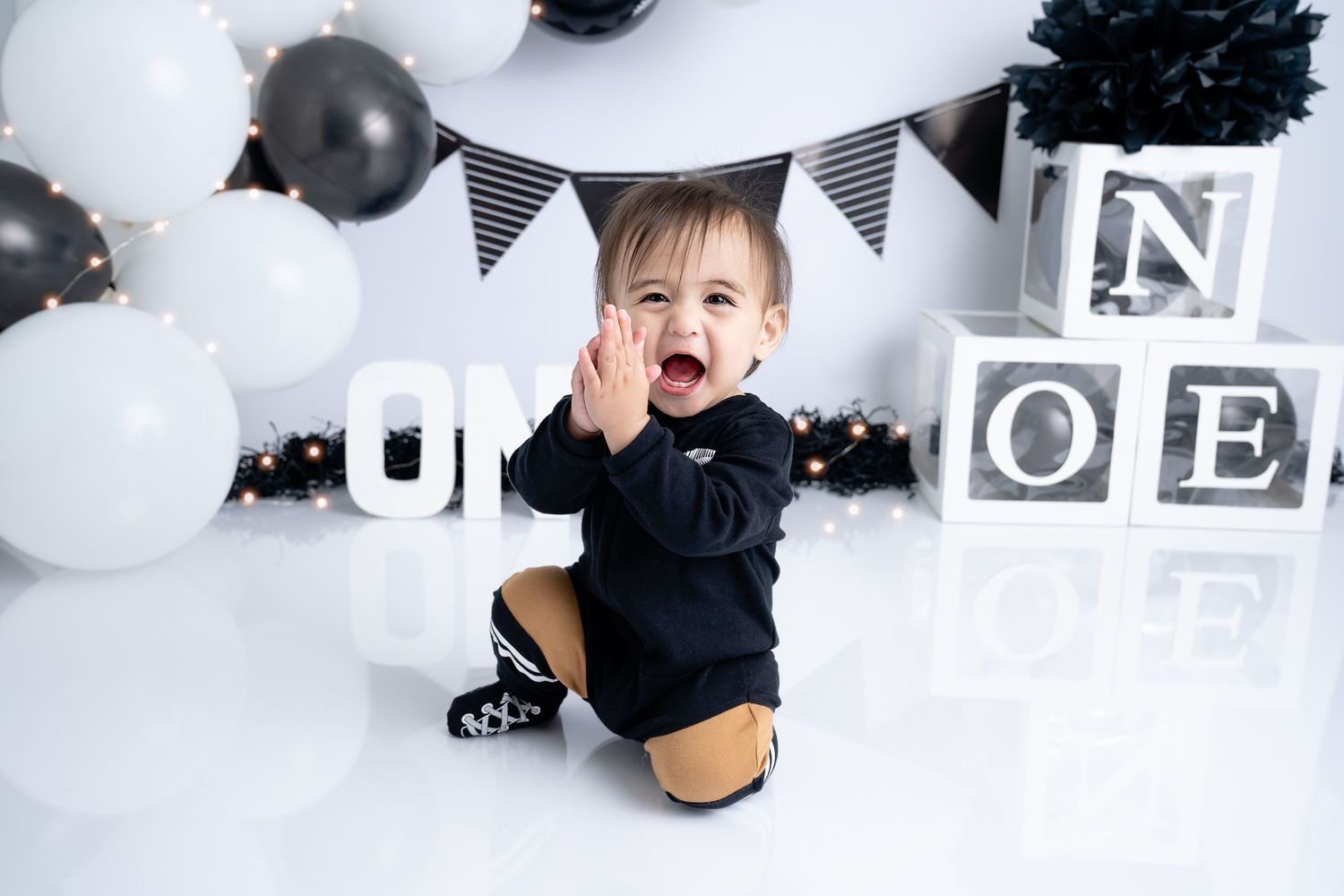 Black and white themed first birthday photo setup with balloons and decorations.