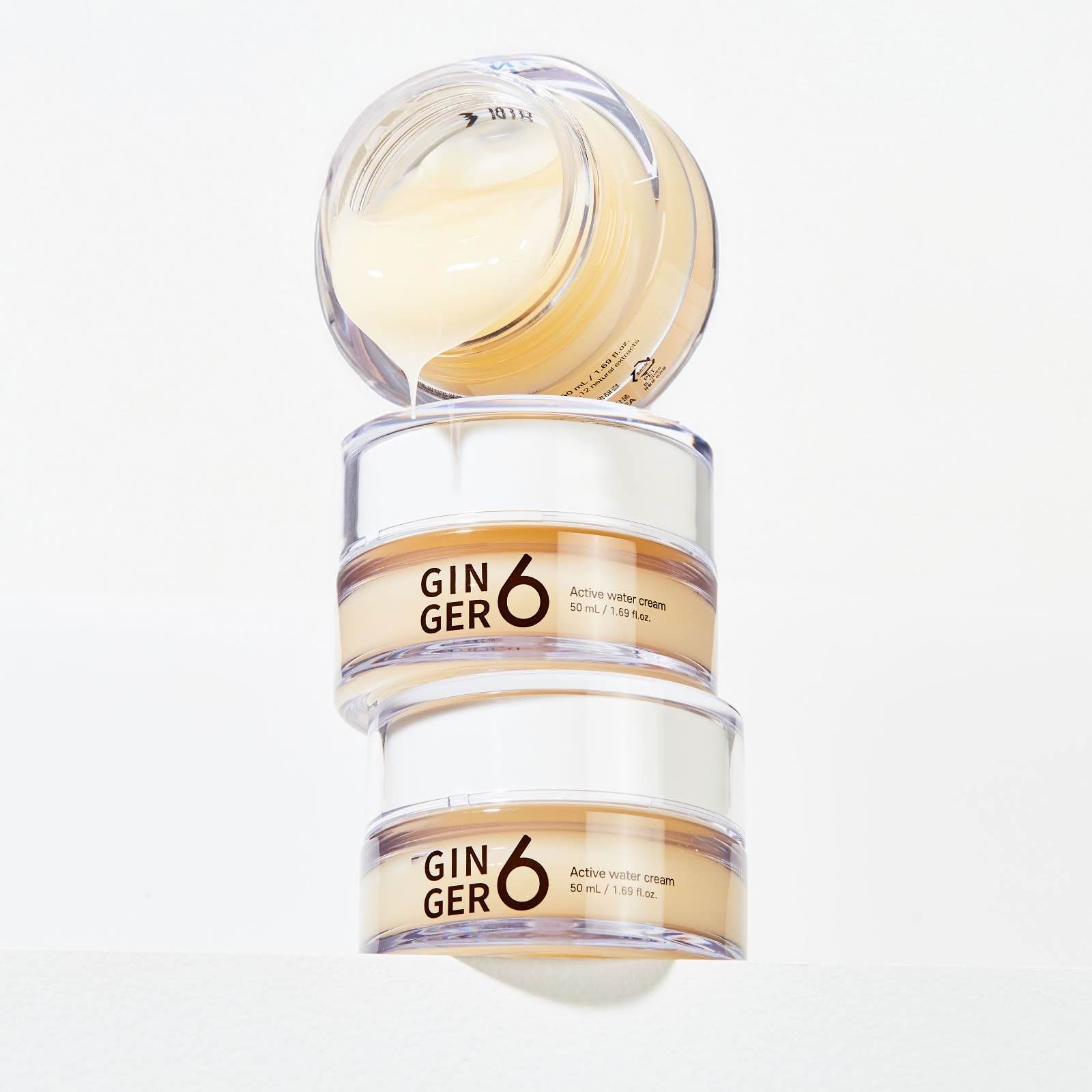 Three stacked jars of Ginger 6 beauty cream against white background.
