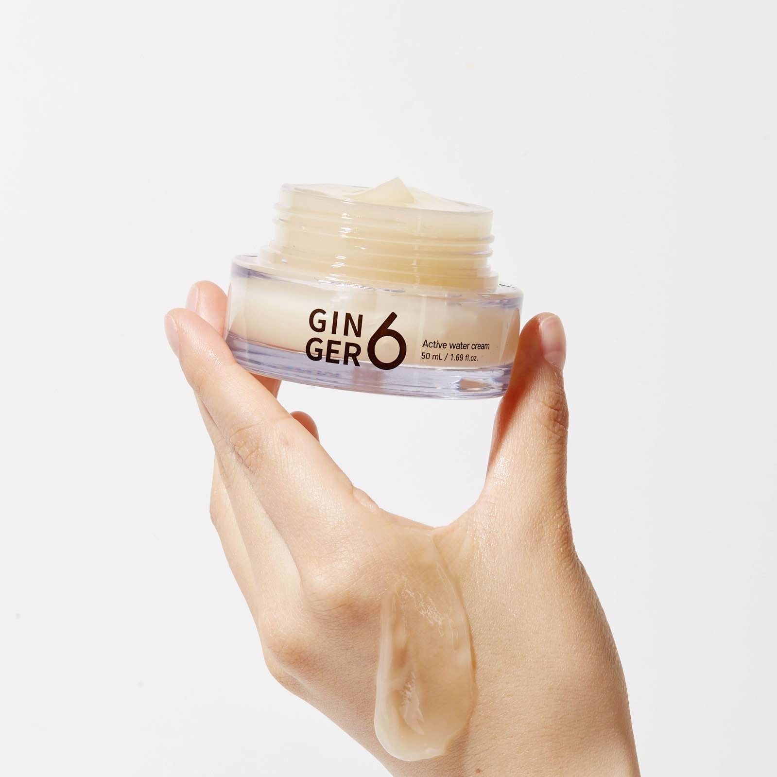 Hand holding jar of Ginger 6 skincare cream against white background.