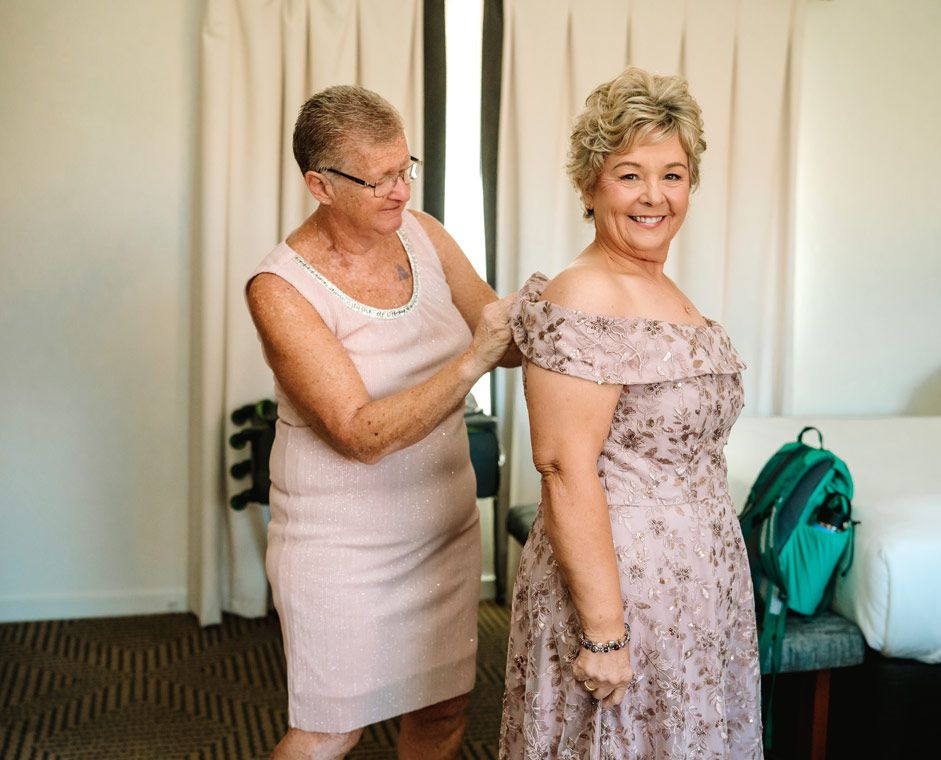 An intimate getting-ready moment showing final dress adjustments in a light-filled room.