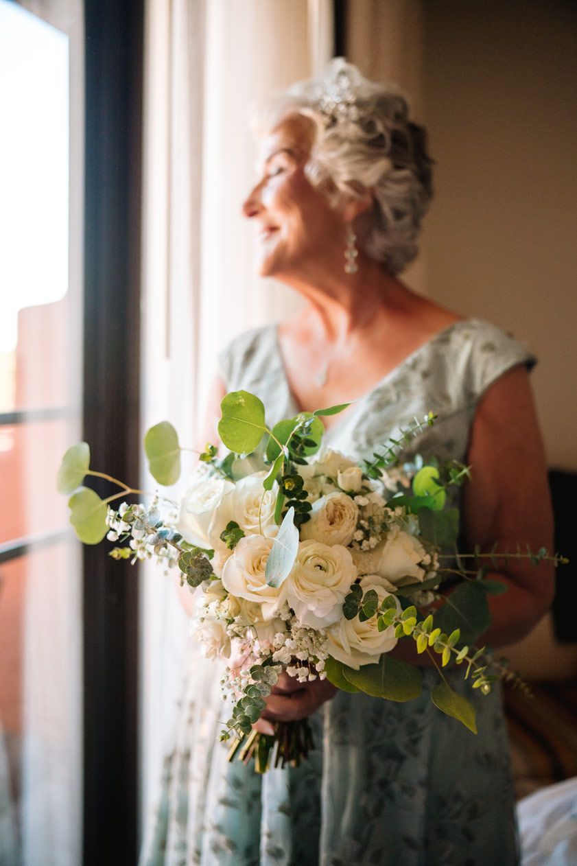 A beautiful bouquet of white roses and greenery by a sunlit window.