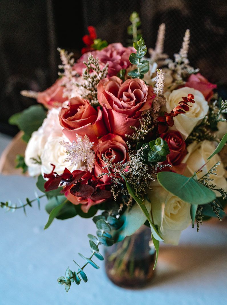 Beautiful wedding bouquet featuring coral roses, white flowers and eucalyptus in a glass vase.