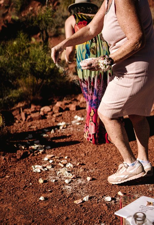 Pink-dressed figure scattering flower petals on Sedona red desert ground.