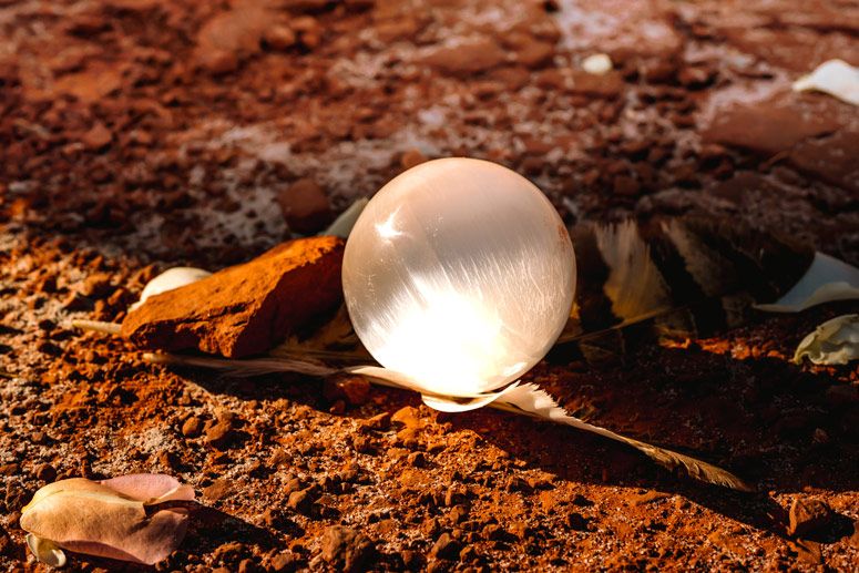 A clear crystal ball rests on Sedona red desert rock with fallen leaves nearby.