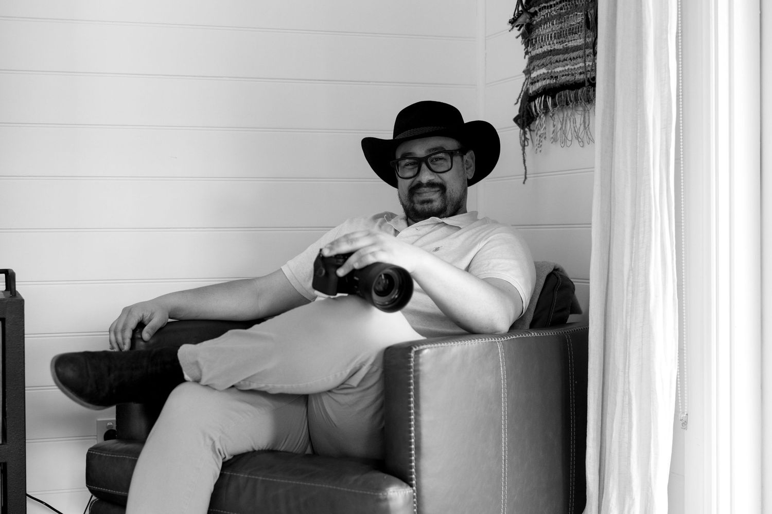 Person relaxing in leather armchair wearing black hat and glasses.