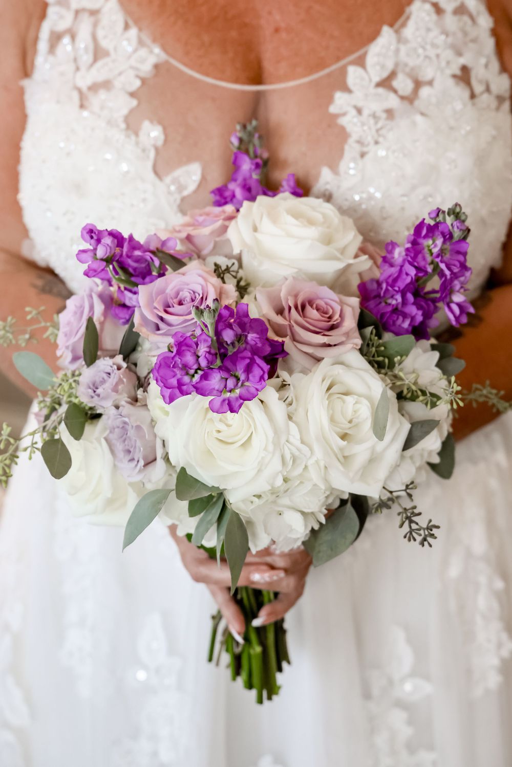 Elegant bridal bouquet with white roses, purple stock flowers, and lavender roses.