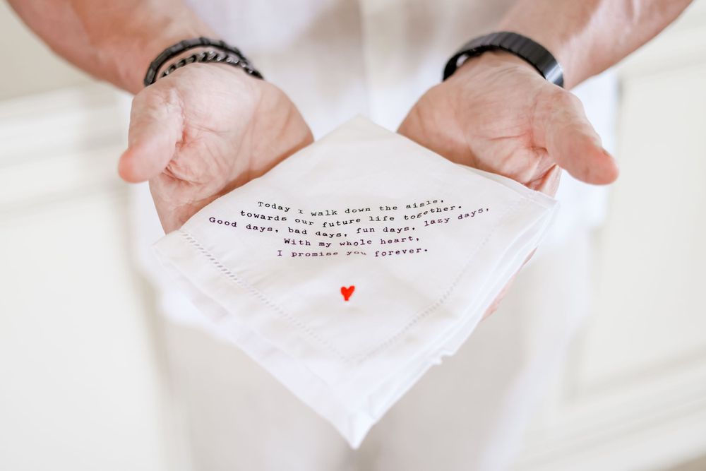 Close-up of hands holding an embroidered wedding handkerchief with a small red heart.
