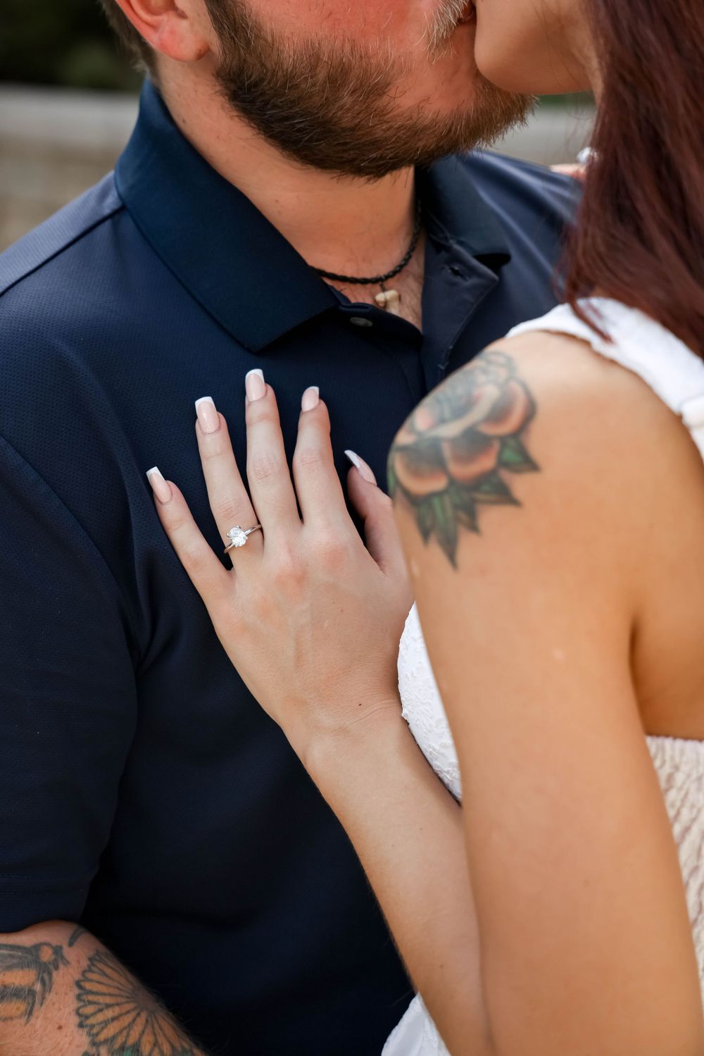 Close-up of hands showing an engagement ring with visible tattoos and formal attire.
