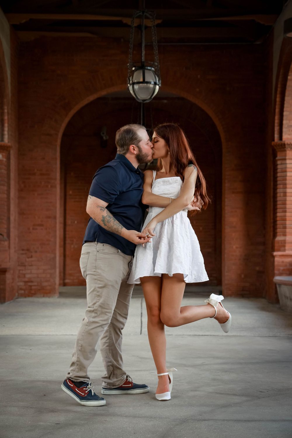A romantic kiss under a brick archway with vintage lighting fixtures.