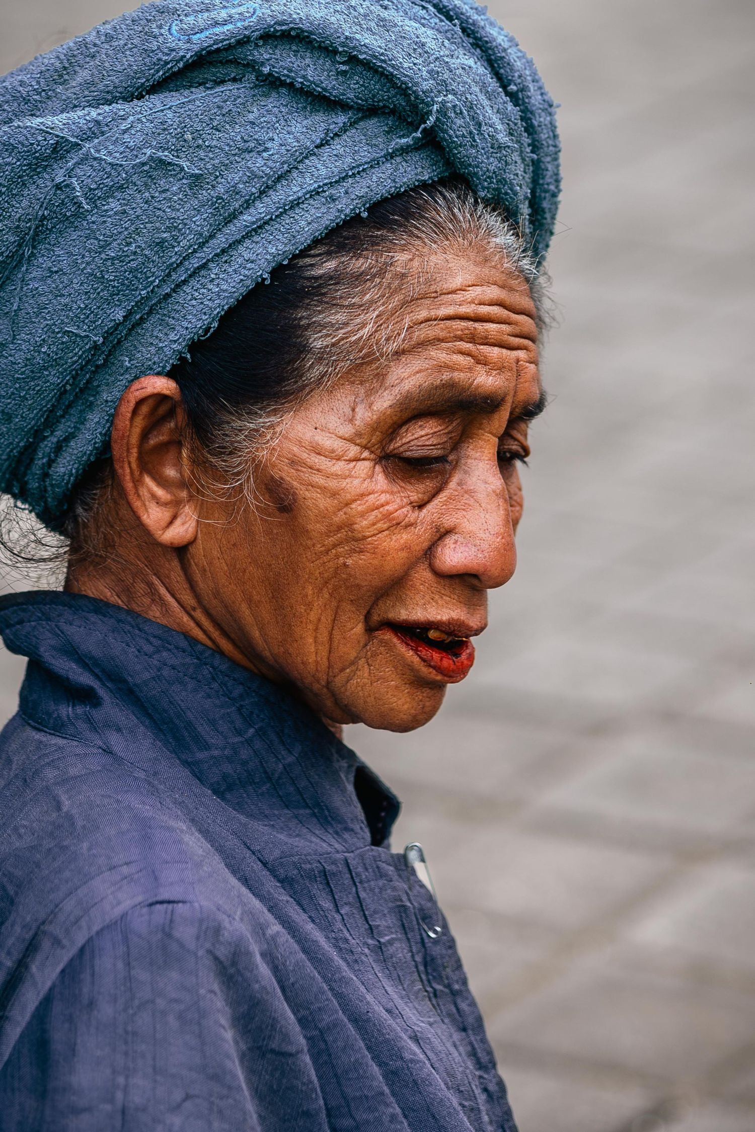 A person wearing traditional blue clothing and headwrap gazes downward.
