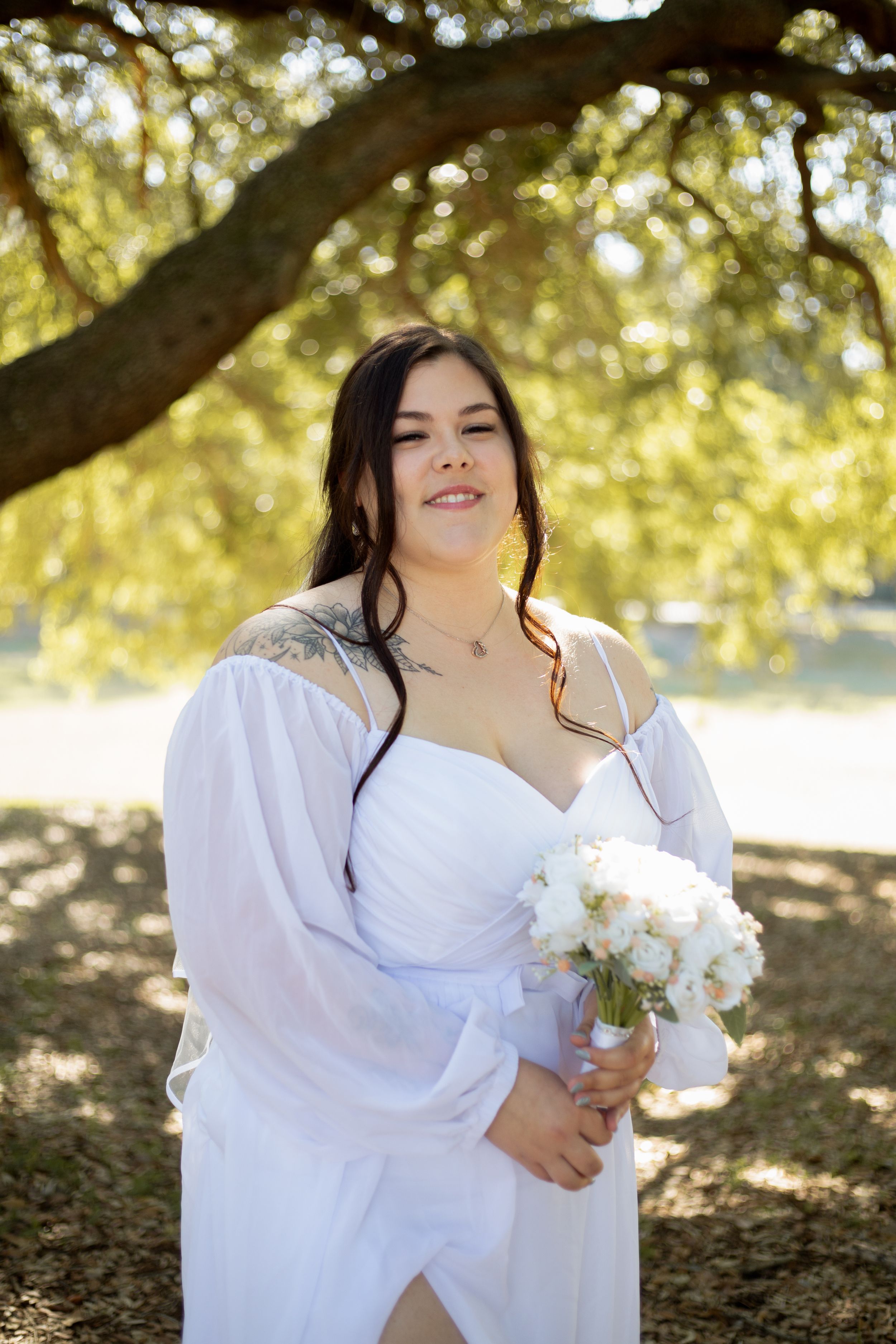 A radiant bridal portrait outdoors holding a white bouquet under golden sunlit trees.