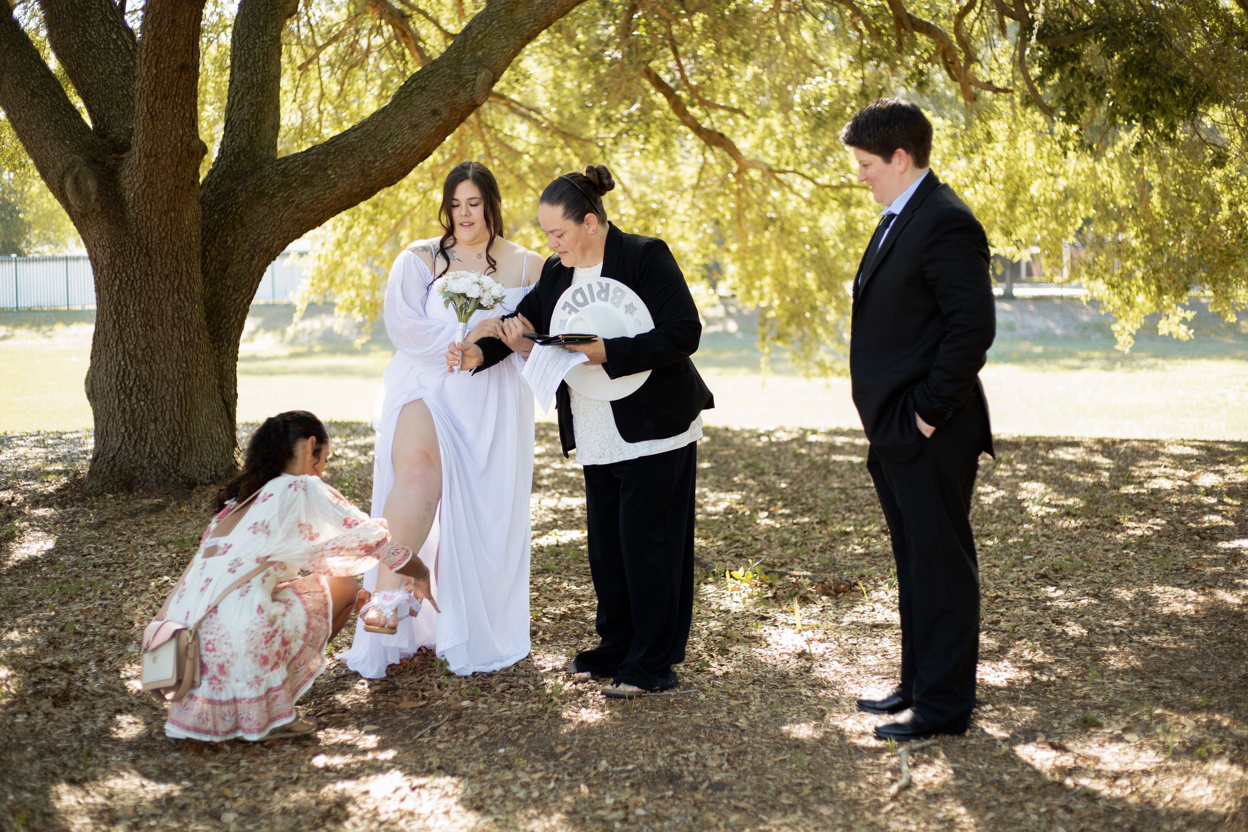 Wedding party helps with final preparations under a sunlit oak tree.