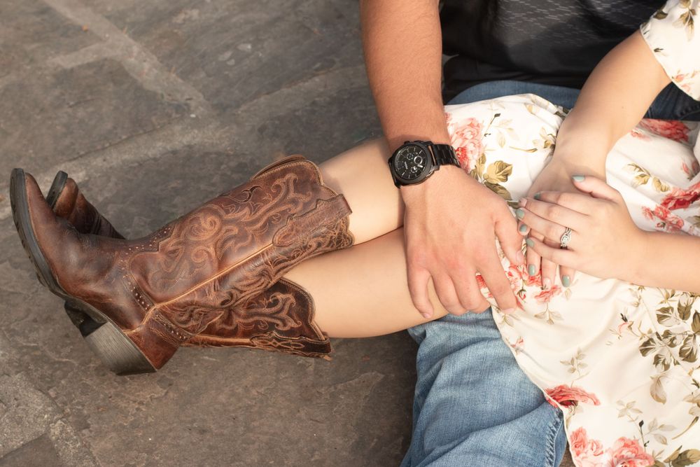 Detail shot of brown cowboy boots and floral dress on stone surface.