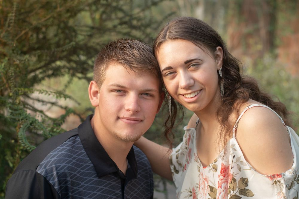 Couple poses together outdoors with greenery and natural setting in background.