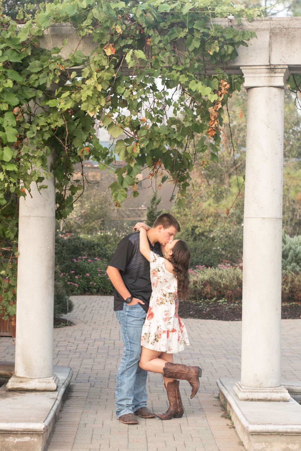 A couple sharing a romantic moment between stone columns with hanging vines in a garden setting.
