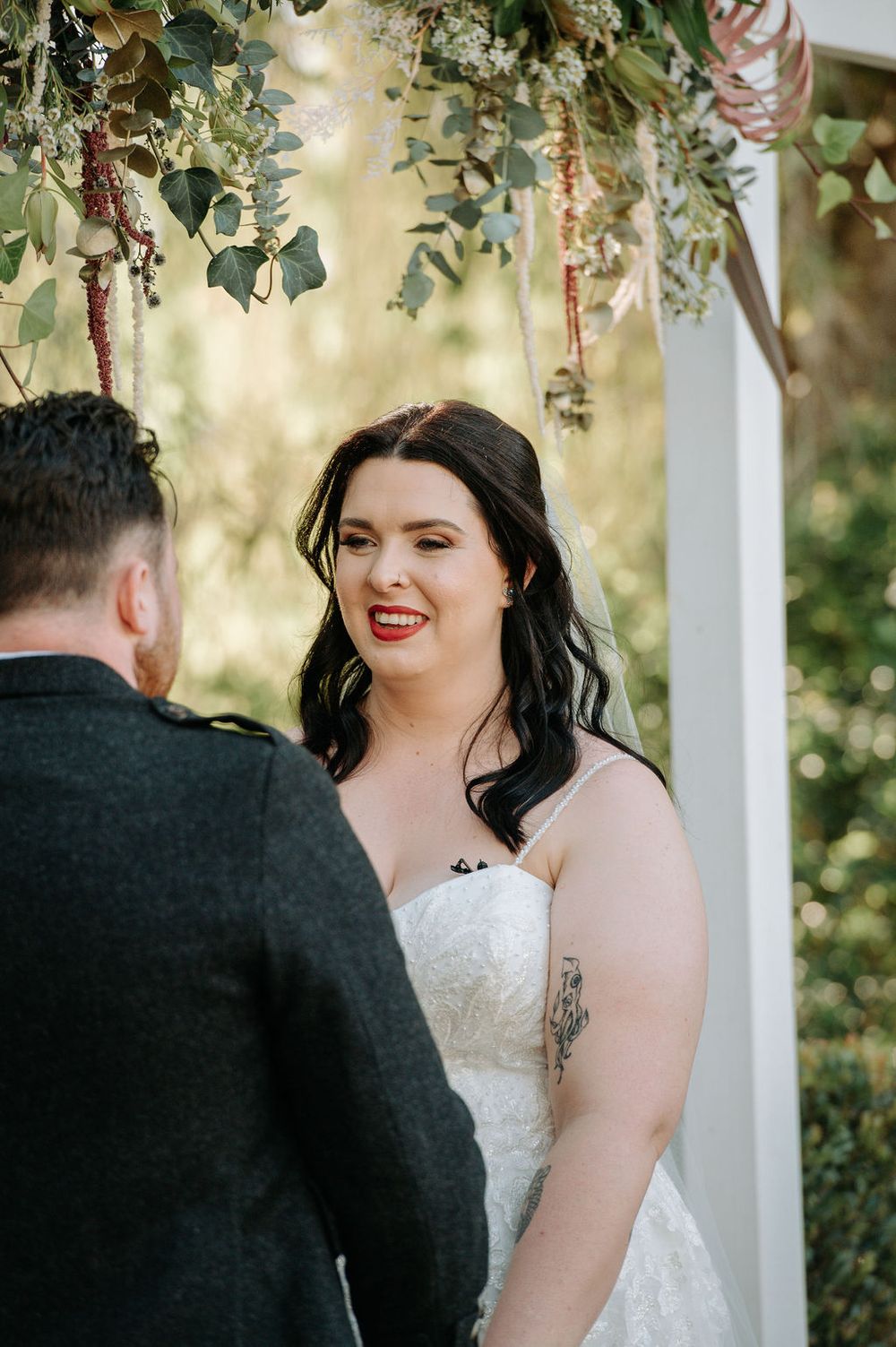 Intimate wedding ceremony under floral arch with hanging greenery and soft lighting.