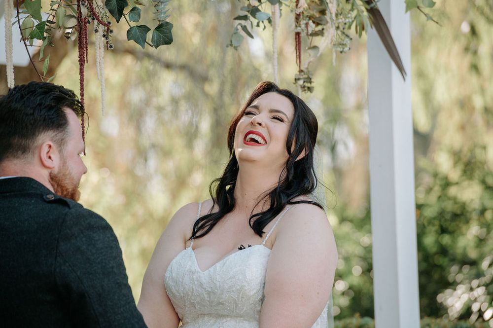 Joyful moment shared under floral wedding arch during outdoor ceremony.