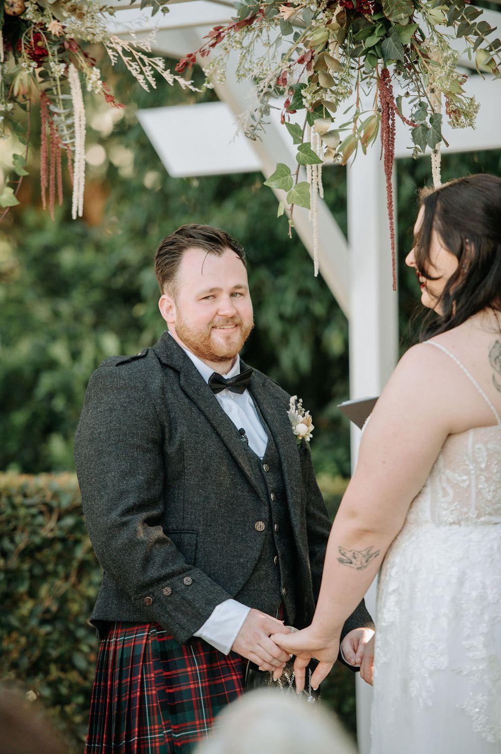 Wedding ceremony under a floral arch with greenery and hanging decorations.