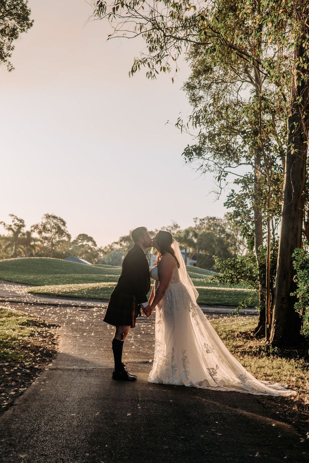 A silhouetted couple shares a romantic moment on a tree-lined path during sunset.