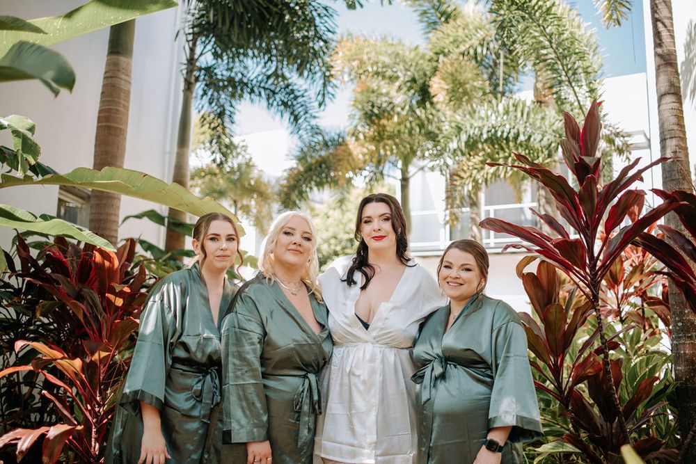 Four people in matching robes stand together among tropical plants at a resort.