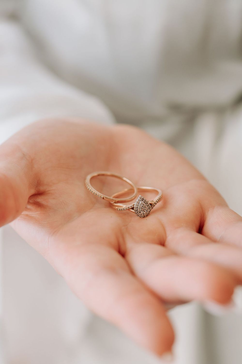 Two delicate wedding rings rest in an open palm, one with a sparkling diamond centerpiece.