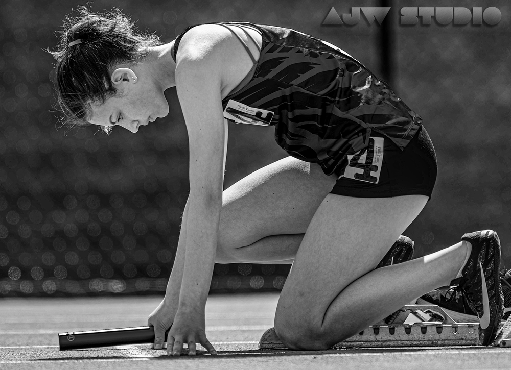 Black and white image of an athlete in starting position on track.