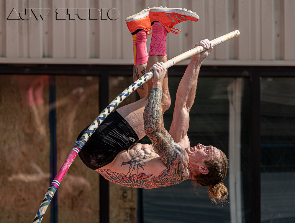 Pole vaulter executing an inverted position while clearing the bar with red shoes.