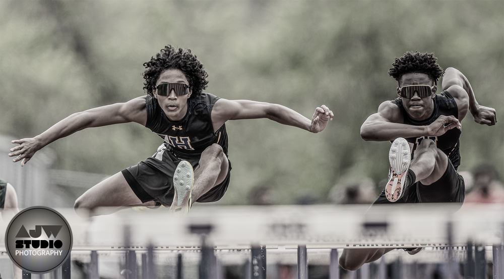 Two athletes clearing hurdles in synchronization during a track competition.