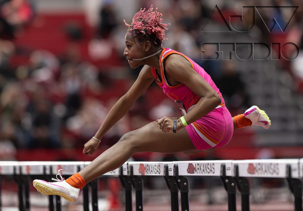 Track athlete in pink uniform jumps over hurdle during competitive race.