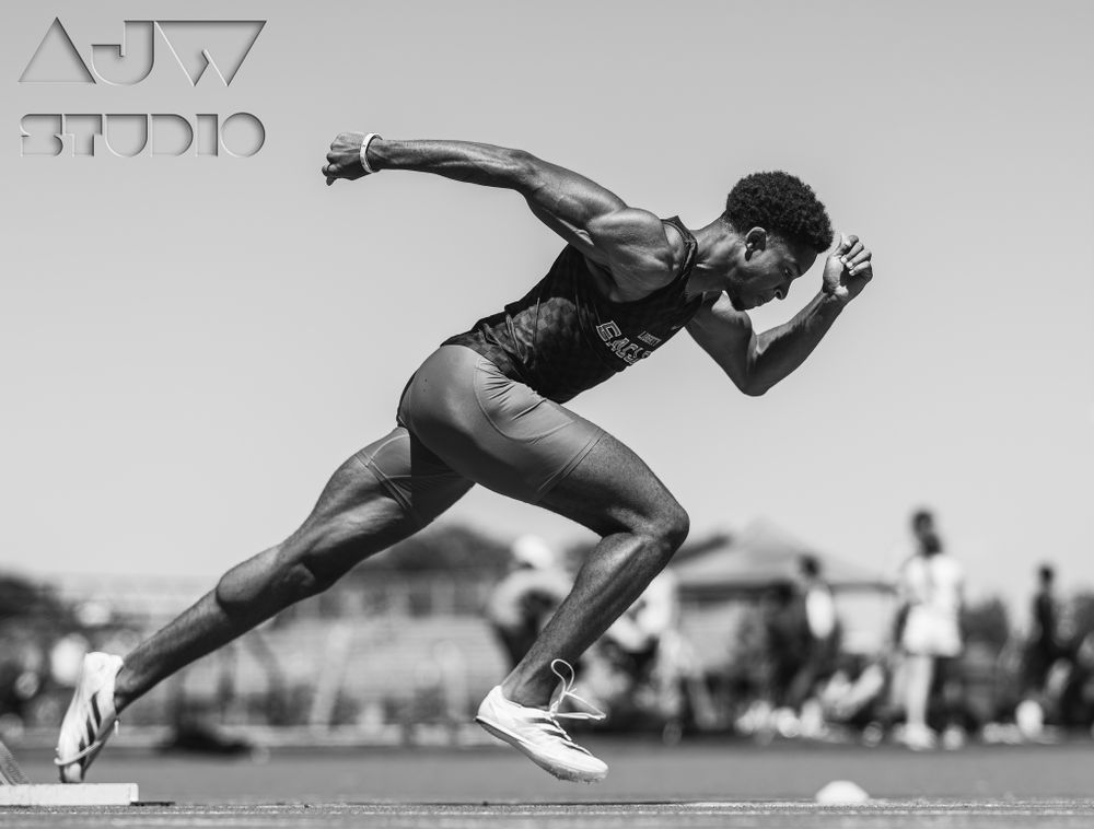Athletic sprinter launches from starting position in dramatic black and white photo.