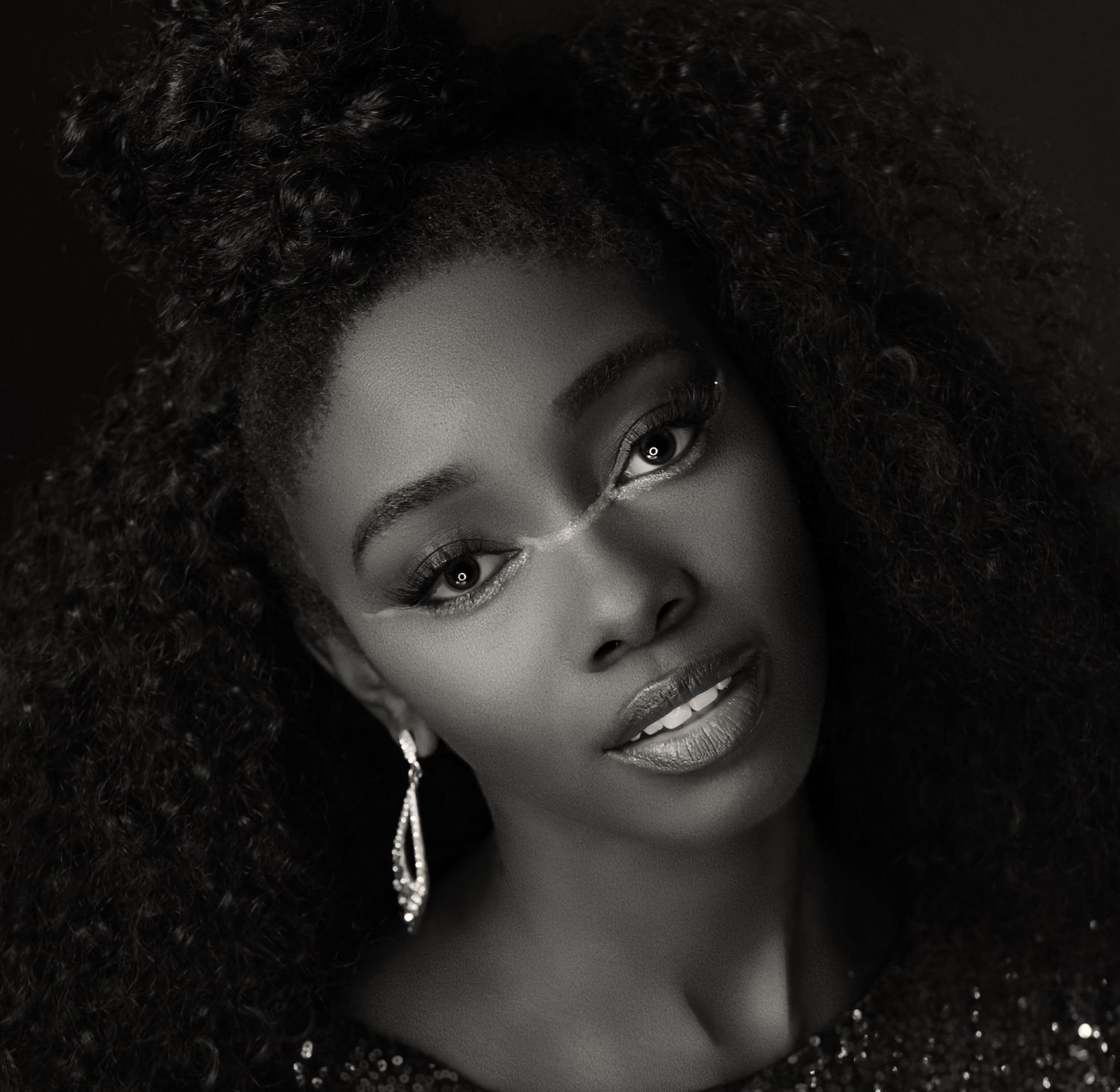 Dramatic black and white beauty portrait with curly hair and statement earrings.