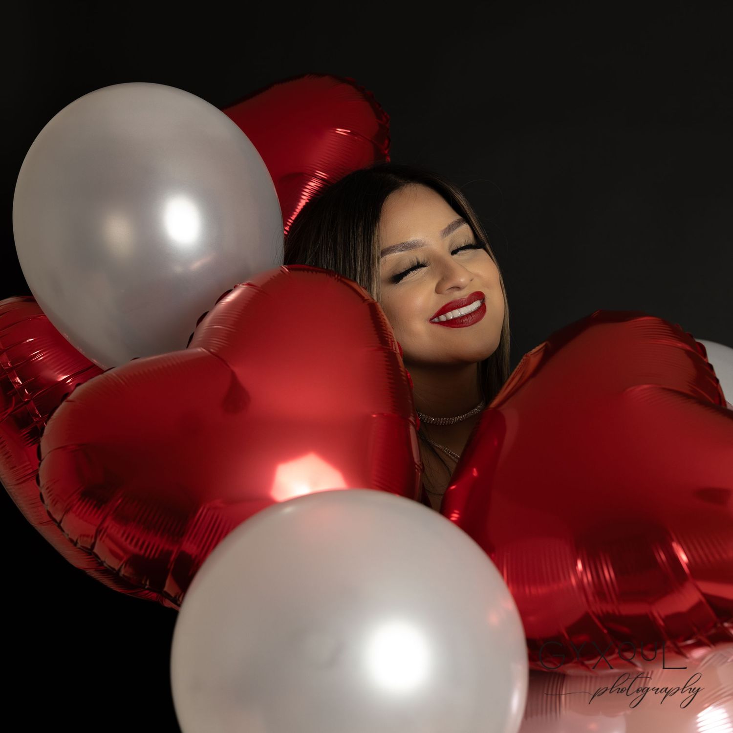 Joyful holiday portrait surrounded by red heart and white round balloons.