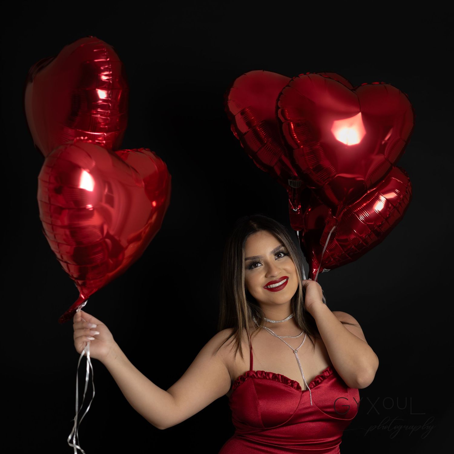Romantic portrait with red satin dress and heart-shaped metallic balloons.