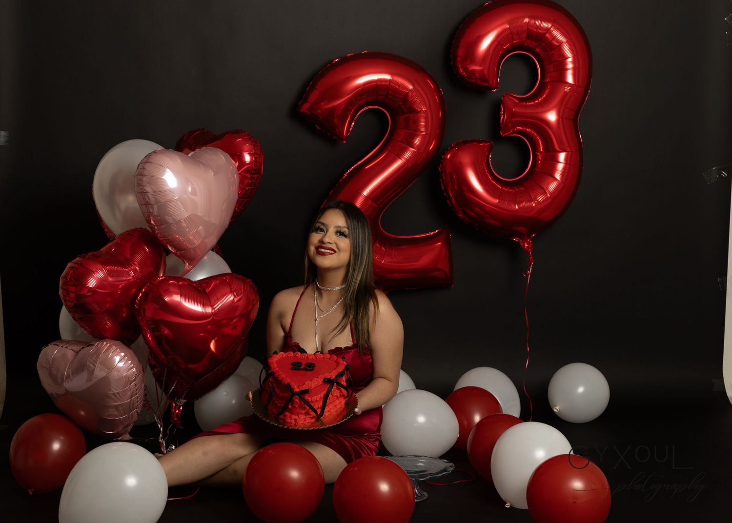 Birthday celebration setup with red balloon numbers showing 23 and decorative heart balloons against dark background.