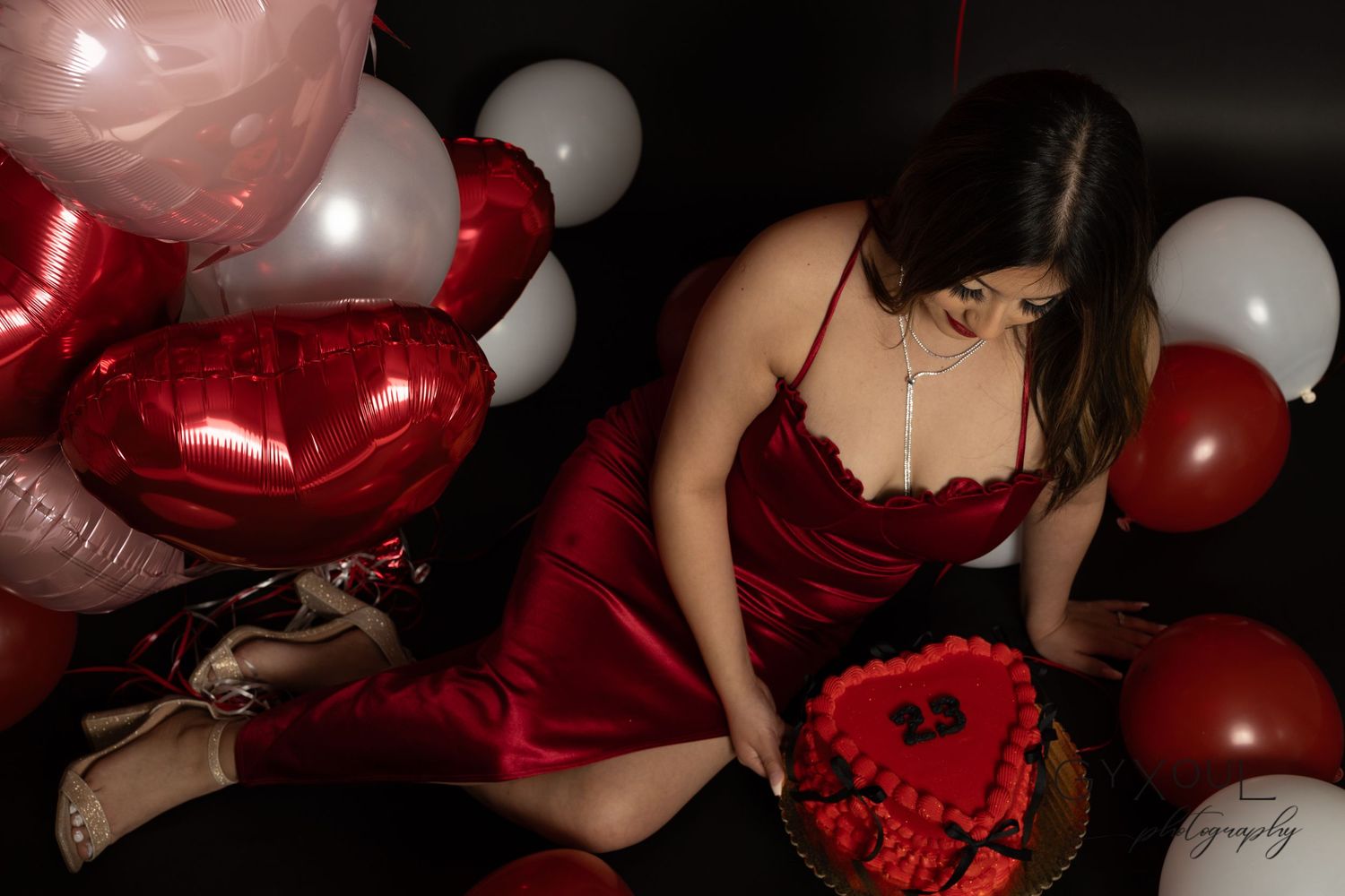 Romantic Valentine's themed photo shoot with red dress and heart balloons.