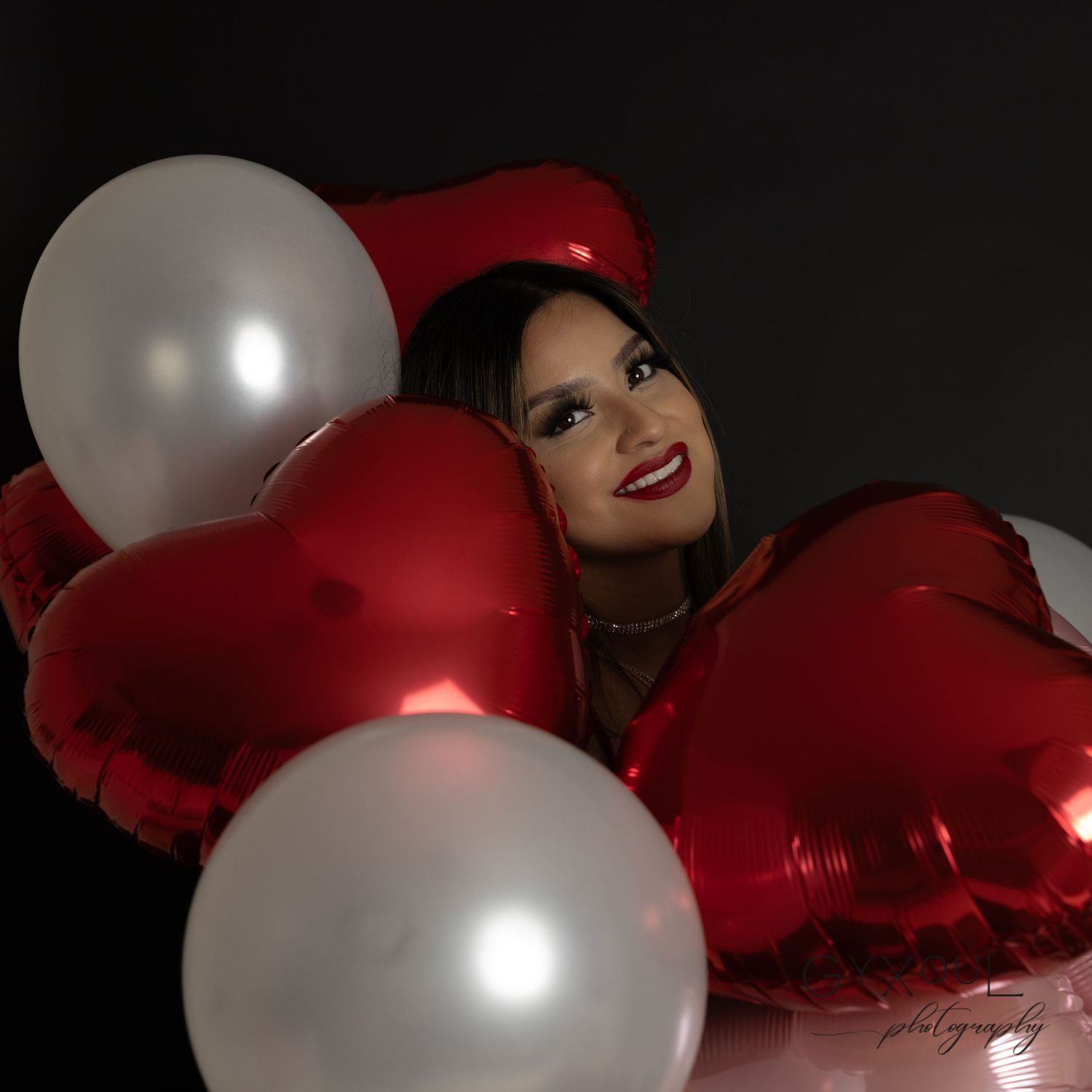 Festive portrait with red and white heart-shaped balloons against dark background.