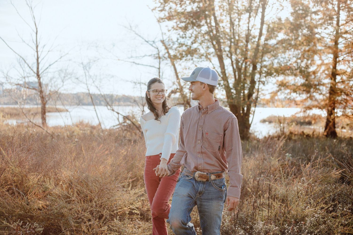 A couple enjoying a sunny autumn day by the water with trees in the background.