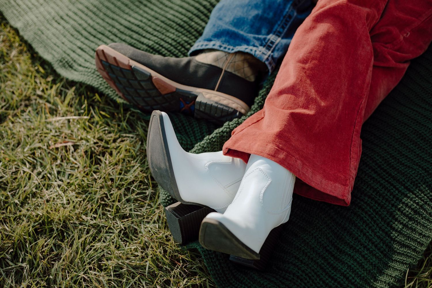 White and brown boots resting on grass and a green blanket.