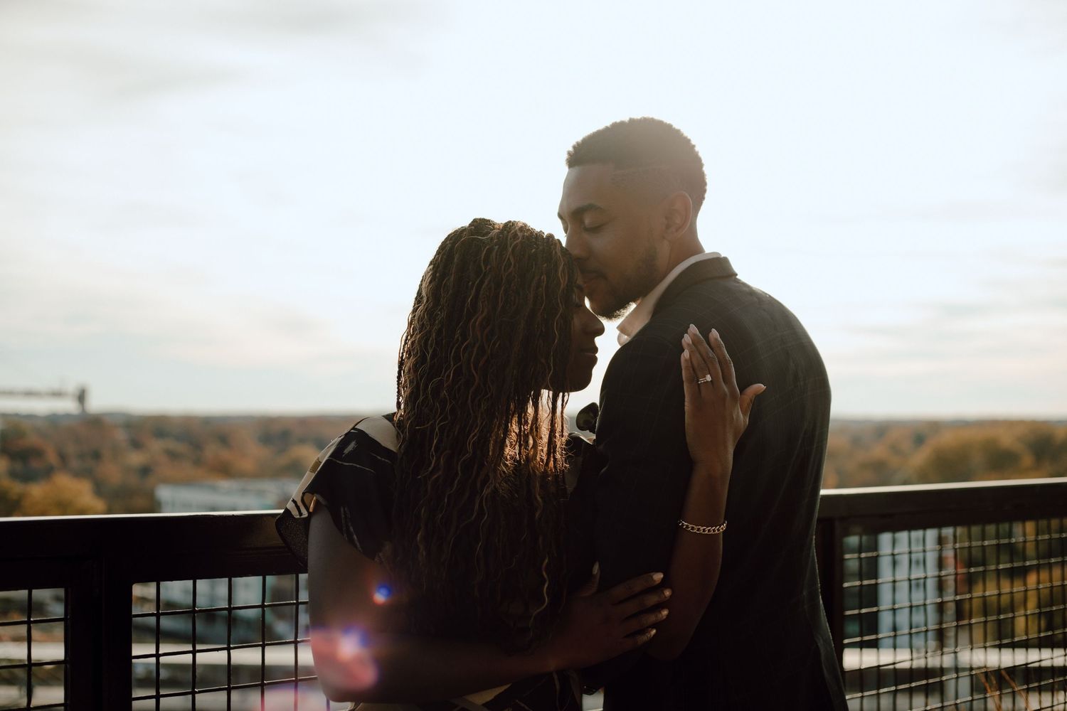 A silhouetted couple shares an intimate moment on a balcony at sunset overlooking a scenic landscape.
