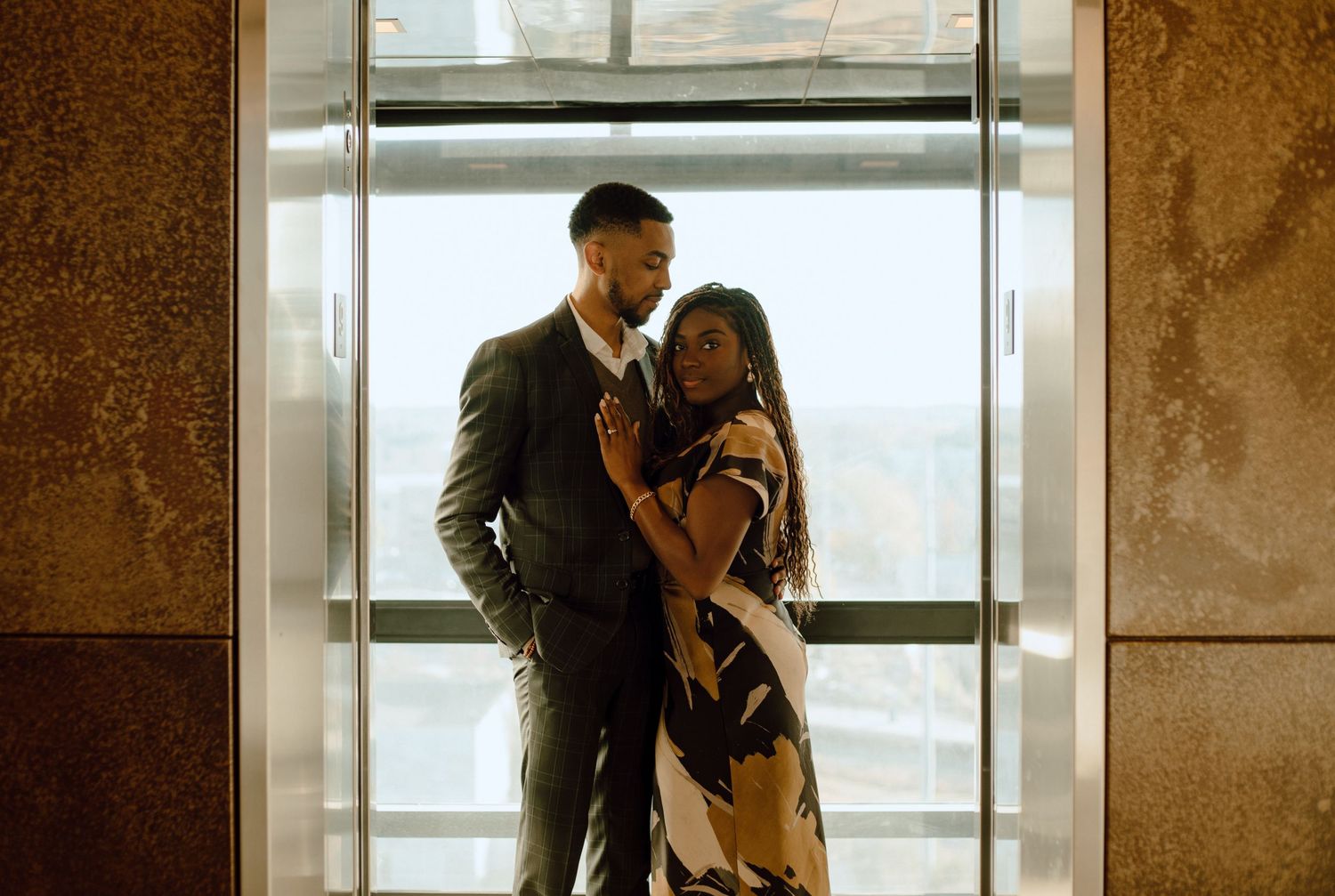 A romantic couple stands intimately by a large window, silhouetted against natural light in an elegant indoor setting.