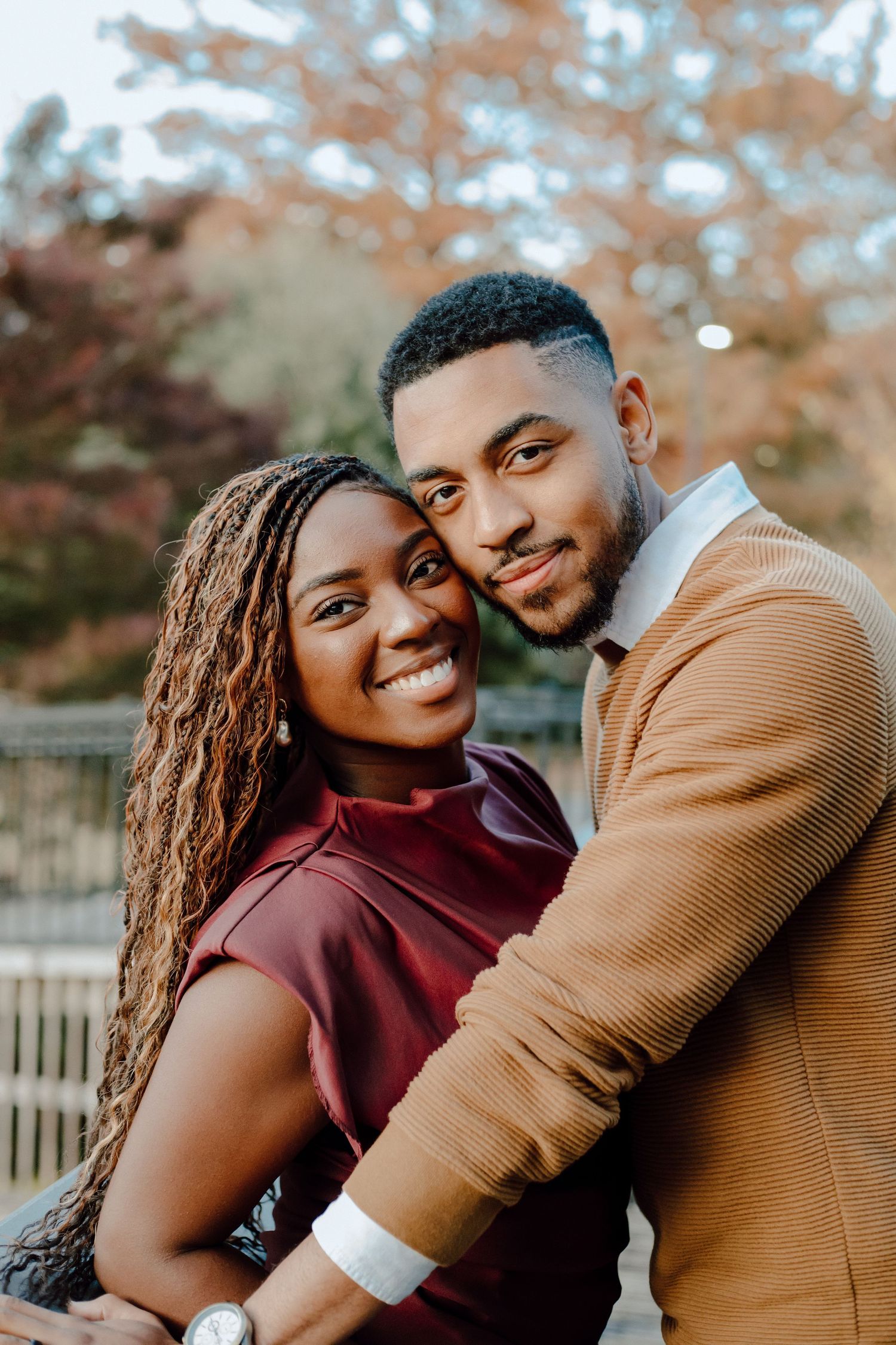 A couple shares an intimate moment outdoors during autumn with warm earth-toned clothing and natural lighting.