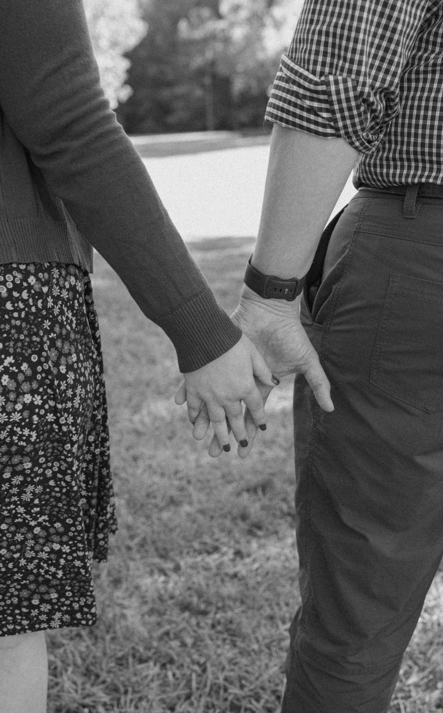 Black and white close-up of couple holding hands outdoors.