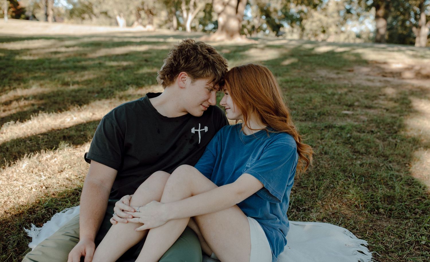 Couple sitting together on a blanket in a sunny park.