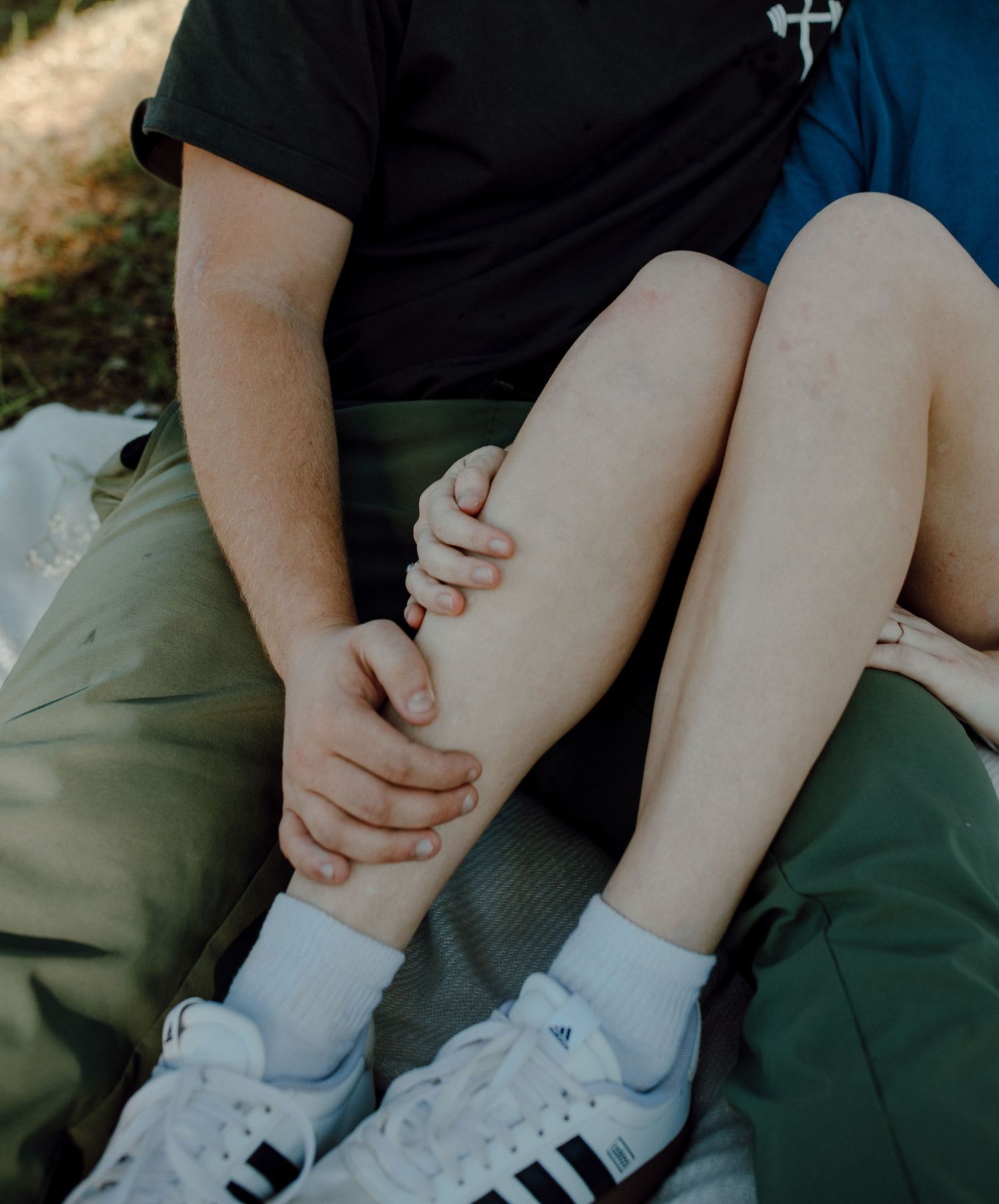 Person wearing black t-shirt and white sneakers sitting on grass.