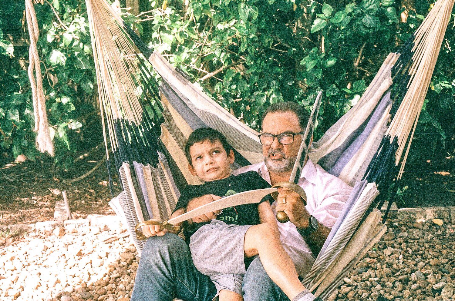 Father and son relaxing together in striped hammock on sunny day.