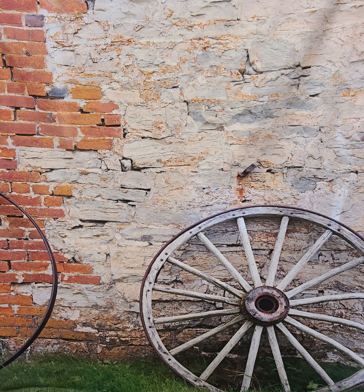 Vintage wagon wheels leaning against weathered brick and stone wall.