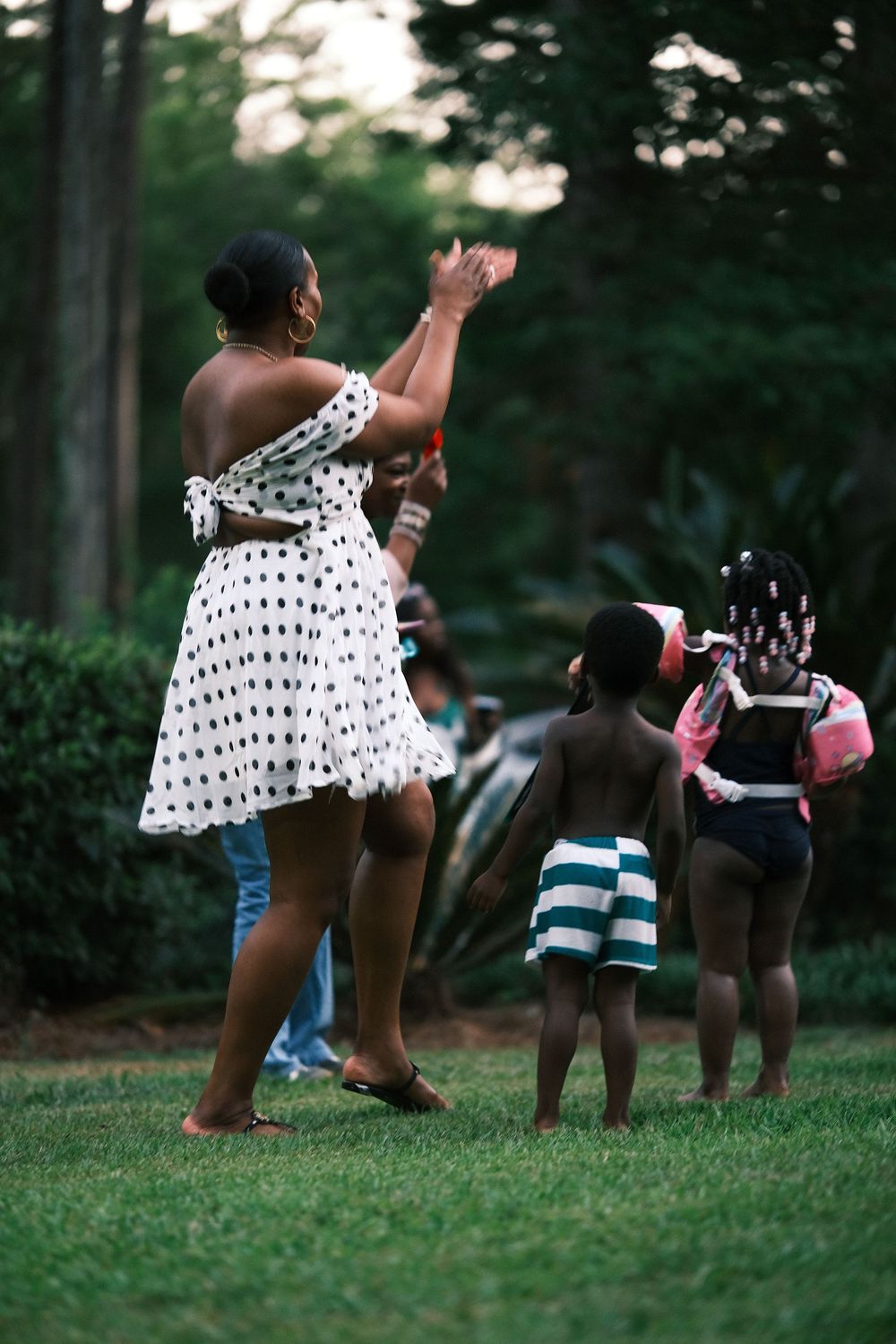 People in summer attire enjoy playing outdoors on a grassy lawn during a late afternoon gathering.