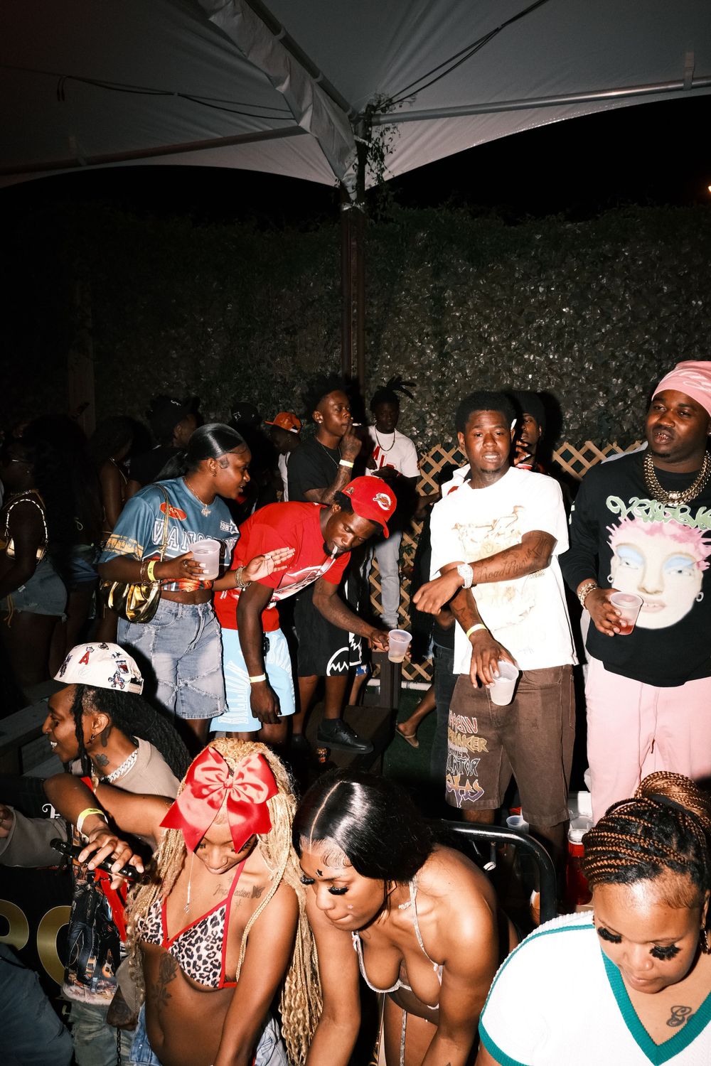 A crowded nightclub party scene with people dancing and socializing under an umbrella at night.