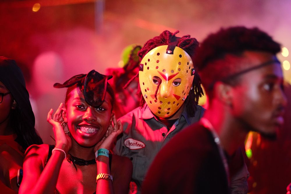 Party scene with person wearing hockey mask in red lighting.