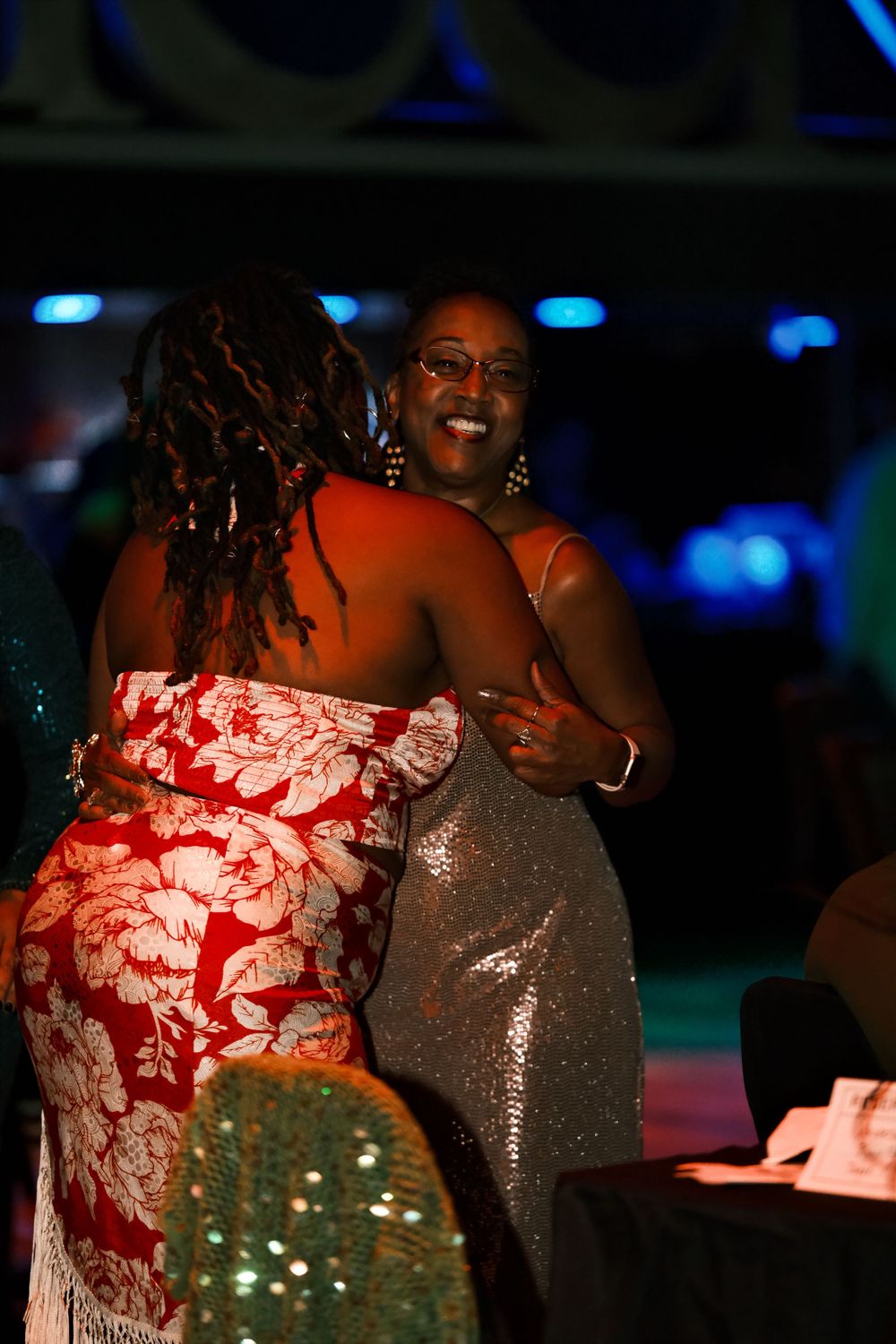 Two partygoers dancing together in elegant dresses under blue lighting.